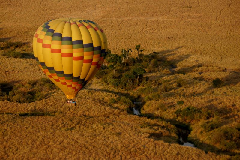 A hot air balloon ascending into the sky over the Masai Mara, showcasing the beautiful landscape and diverse wildlife from above.